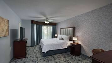 Ein Hotelzimmer mit einem großen Bett, einem Schreibtisch, einem Stuhl, einem Fernseher und einem Deckenventilator.