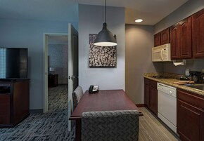 A compact hotel room with a dining table, a microwave, a sink, and a television.