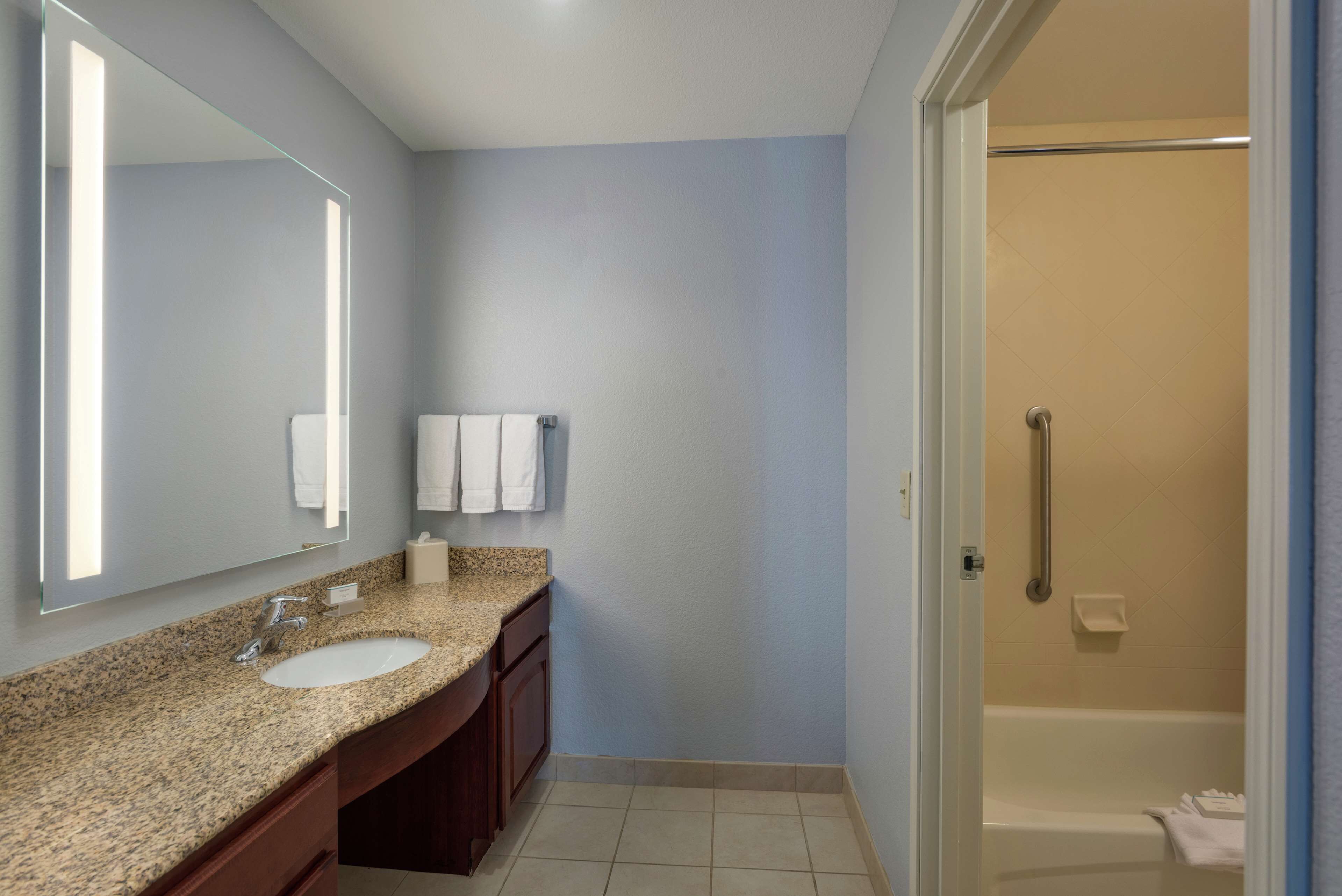 A bathroom with a granite countertop sink, a large mirror, and a walk-in shower.