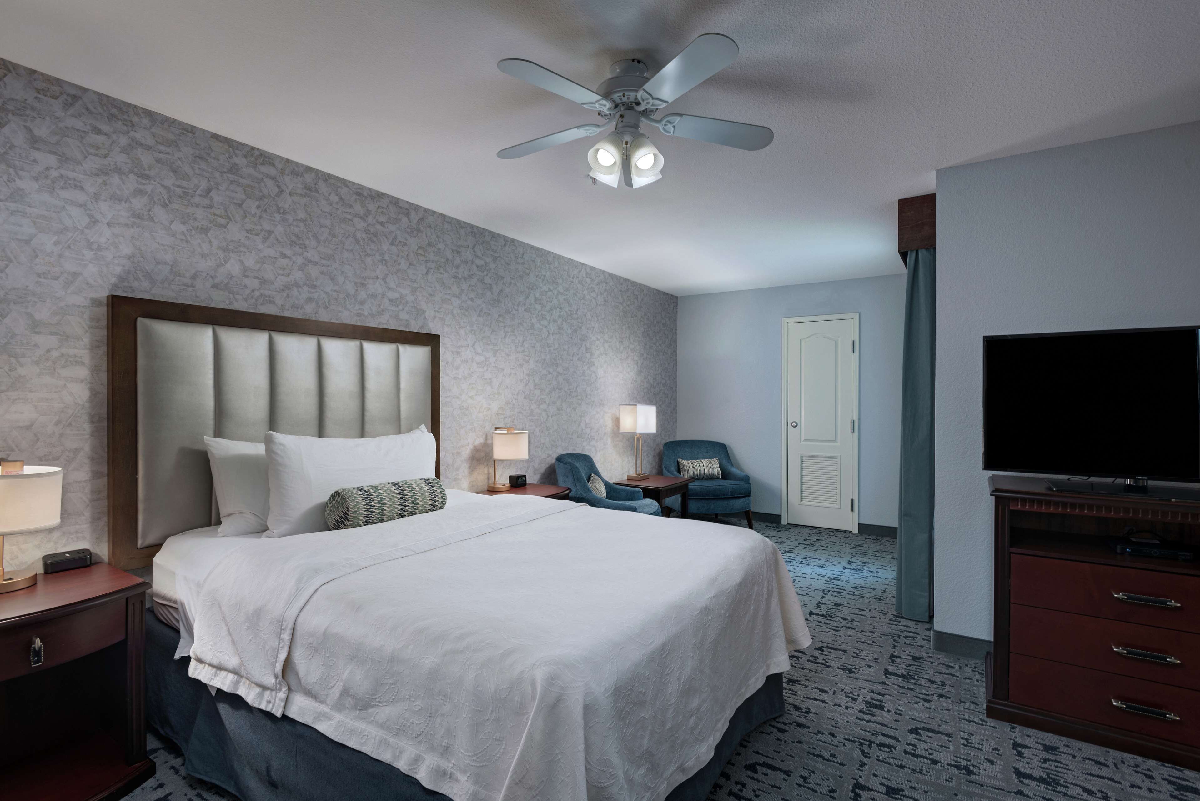 Ein Hotelzimmer mit einem großen Bett, einem Deckenventilator, einem Fernseher, einem Schreibtisch und einem Stuhl.