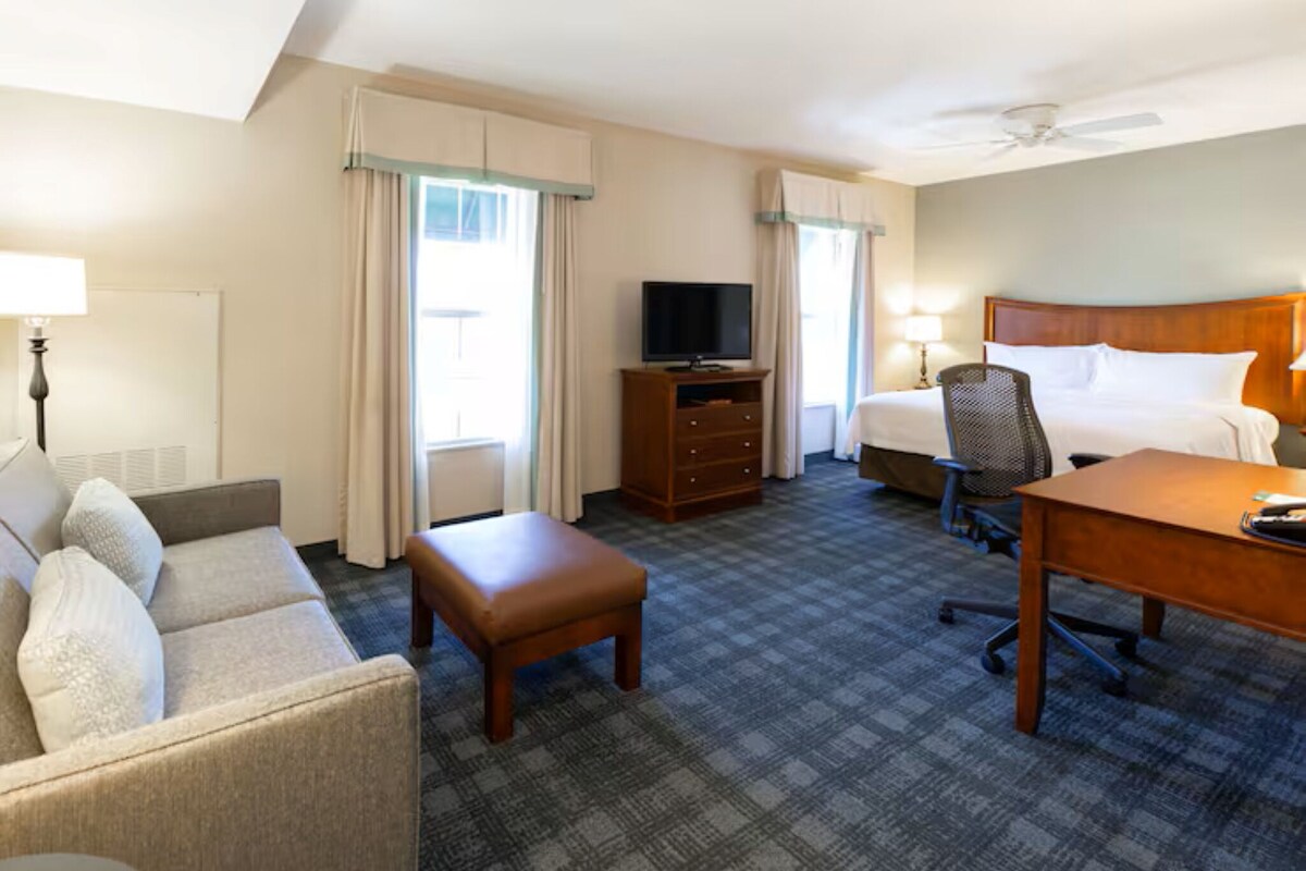 A hotel room with a bed, a desk, a chair, a sofa, a television, and a lamp.