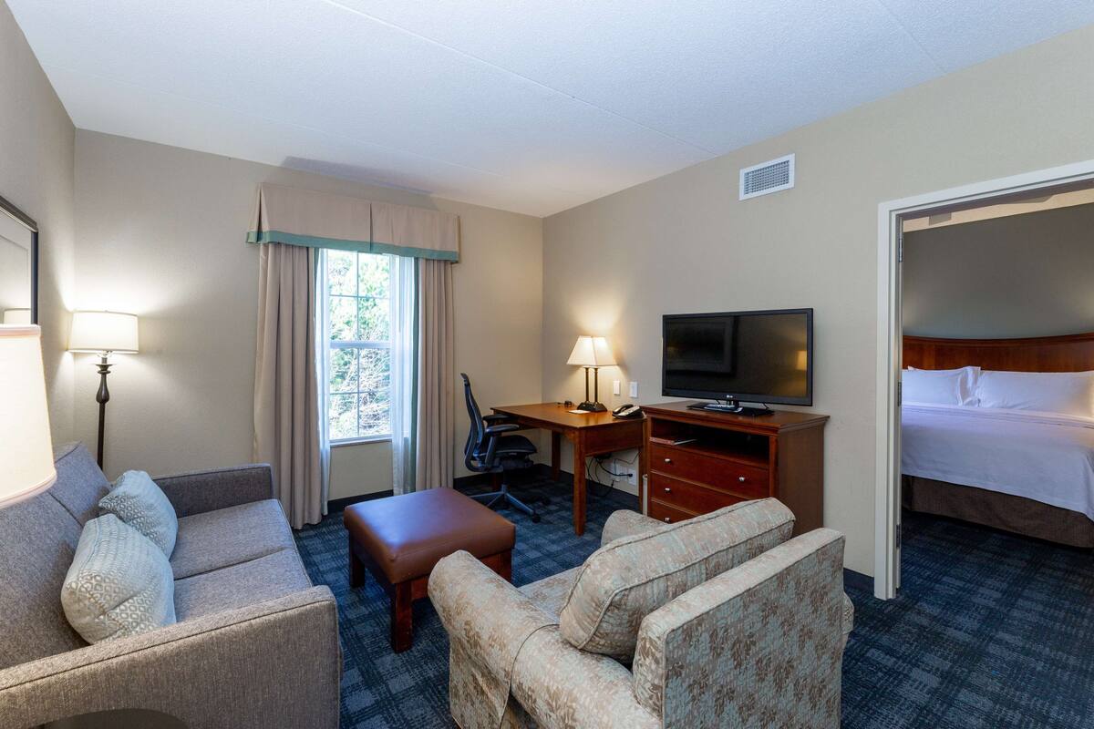 Une chambre d’hôtel comprenant un lit, un bureau avec une télévision, un canapé, un fauteuil et une fenêtre avec des rideaux.