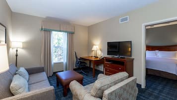 A hotel room with a bed, a desk with a TV, a sofa, a chair, and a window with curtains.