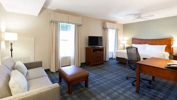 Una habitación de hotel con cama, escritorio, silla, televisión y sofá.
