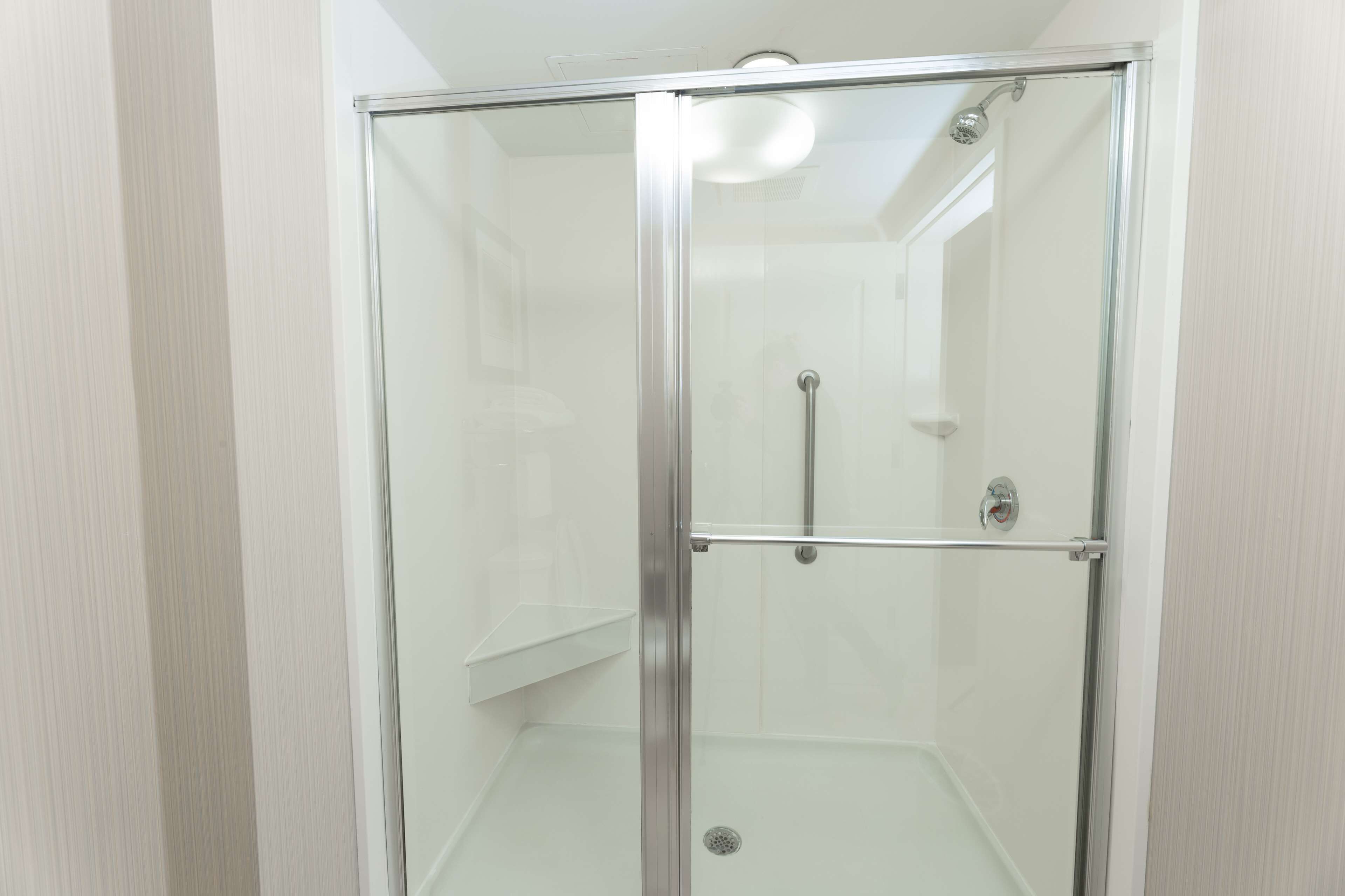 A glass-enclosed shower with a metal frame, a visible showerhead, and a metal handrail.