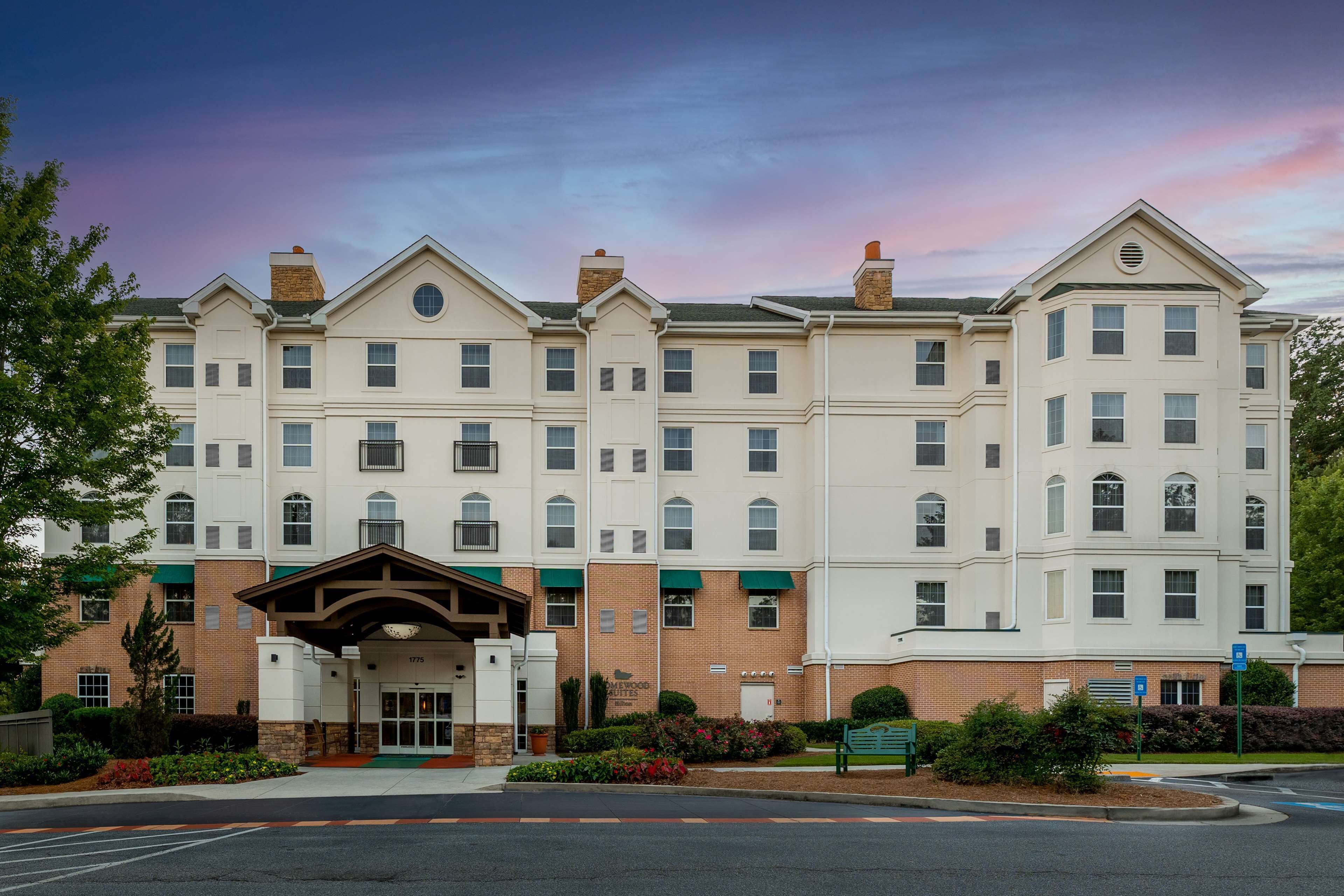 A multi-story hotel with a central entrance, brick facade, and a landscaped front yard.