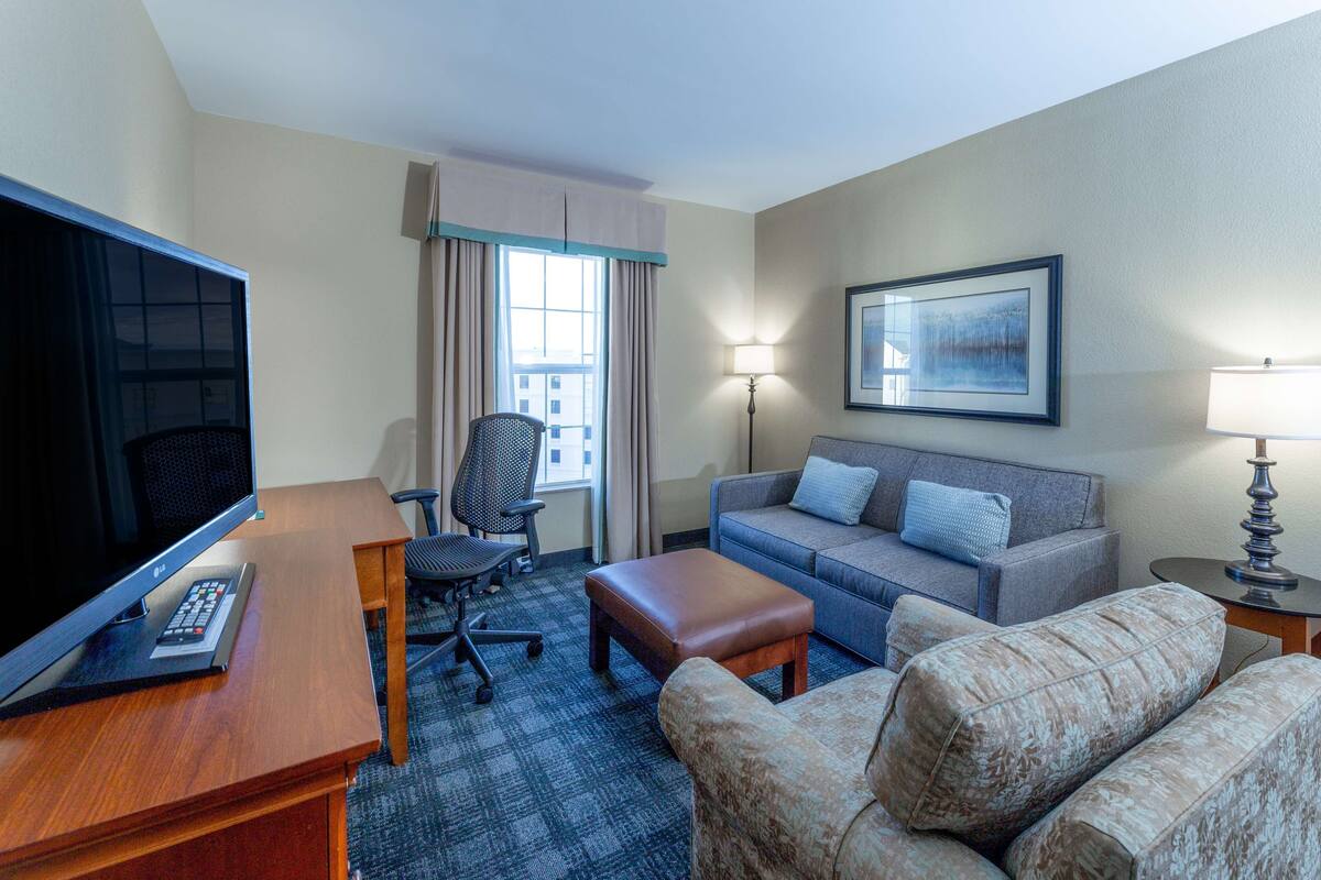 Une chambre d’hôtel équipée d’une télévision à écran plat, d’un canapé, d’un fauteuil, d’un bureau et d’une lampe.