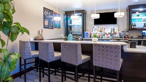 Uma área de bar com quatro banquetas, um balcão com diversos tipos de bebidas e uma televisão fixada na parede.