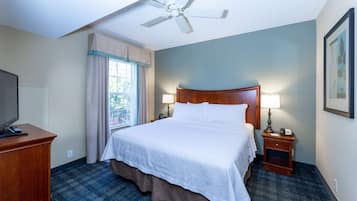 A hotel room with a large bed, a desk, a ceiling fan, a window with curtains, and a framed picture on the wall.