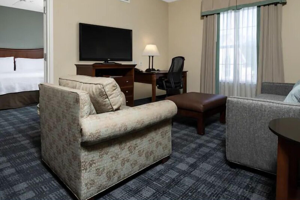 A hotel room with a bed, a sofa, a desk with a chair, a television, and a window with curtains.