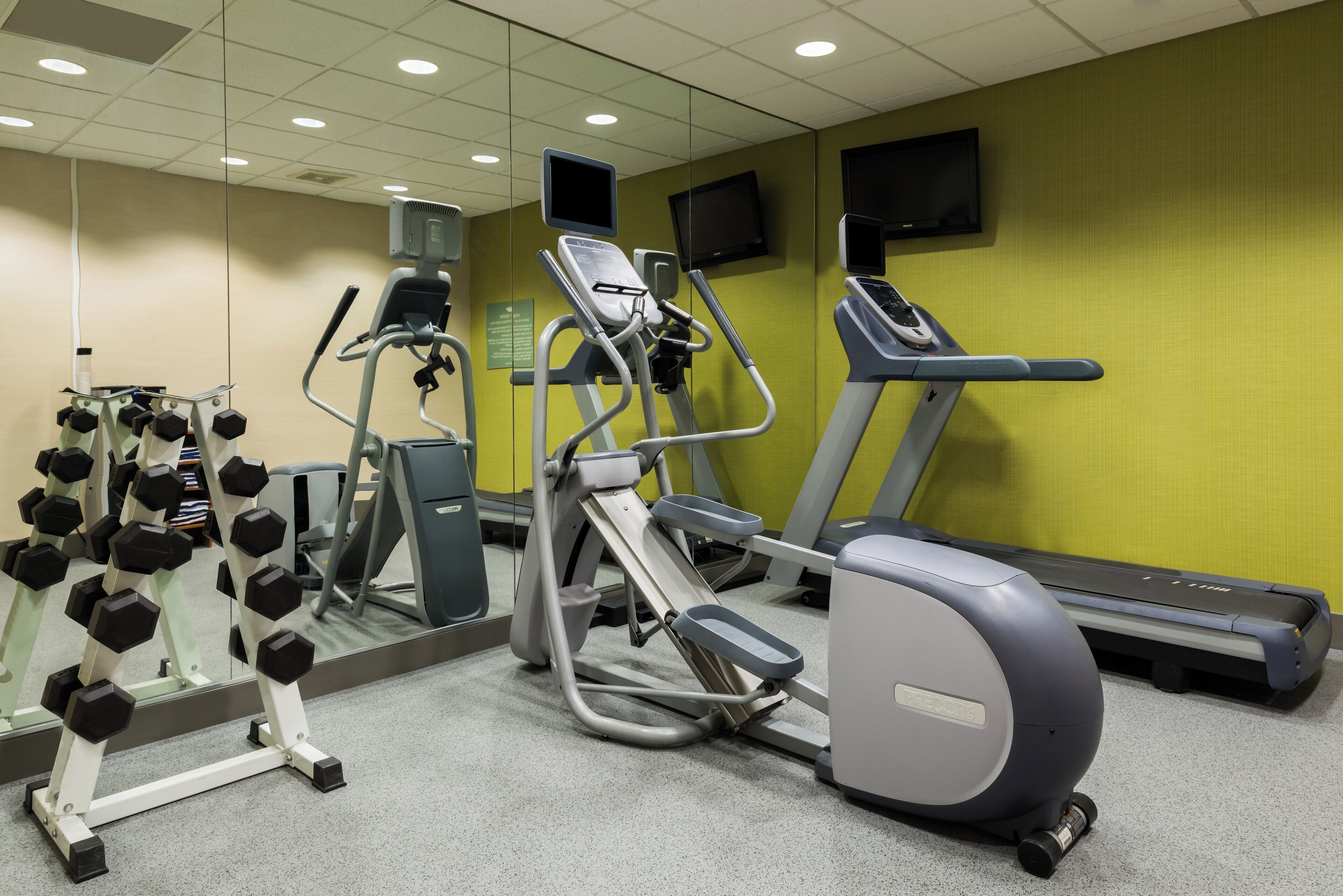 A gym with exercise equipment including treadmills, an elliptical, and dumbbells.