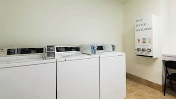 A laundry area with three washers and dryers, a soap and bleach dispenser, and a sign indicating the use of softeners.
