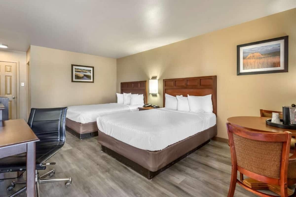 A hotel room with two beds, a desk, a chair, and a dining table.