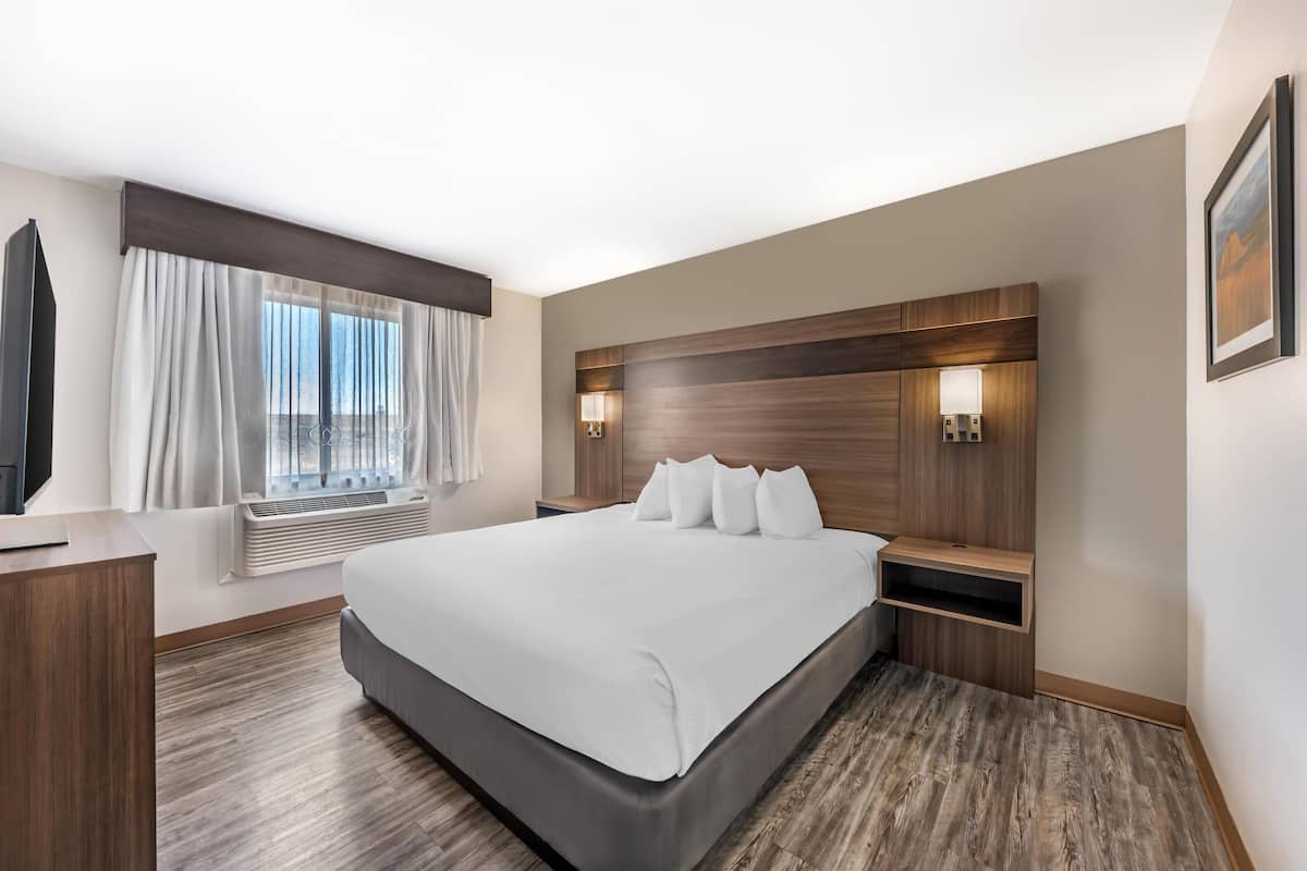 A modern hotel room with a large bed, a flat-screen TV, a desk, and a window with curtains.