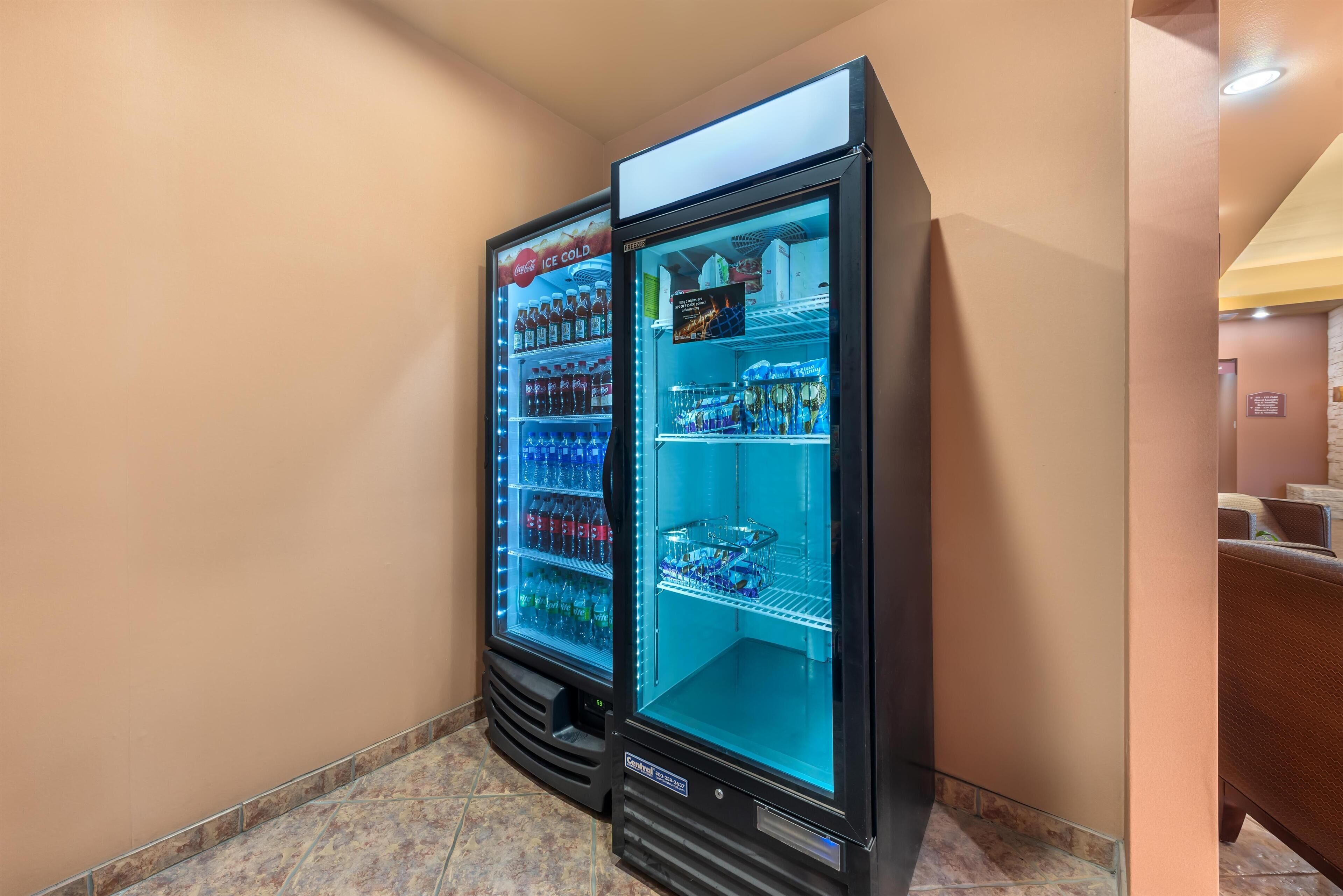 Two vending machines in a hallway with tiled flooring and beige walls.