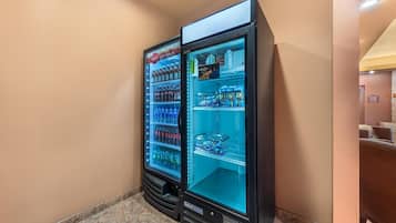 Two vending machines in a hallway with tiled flooring and beige walls.