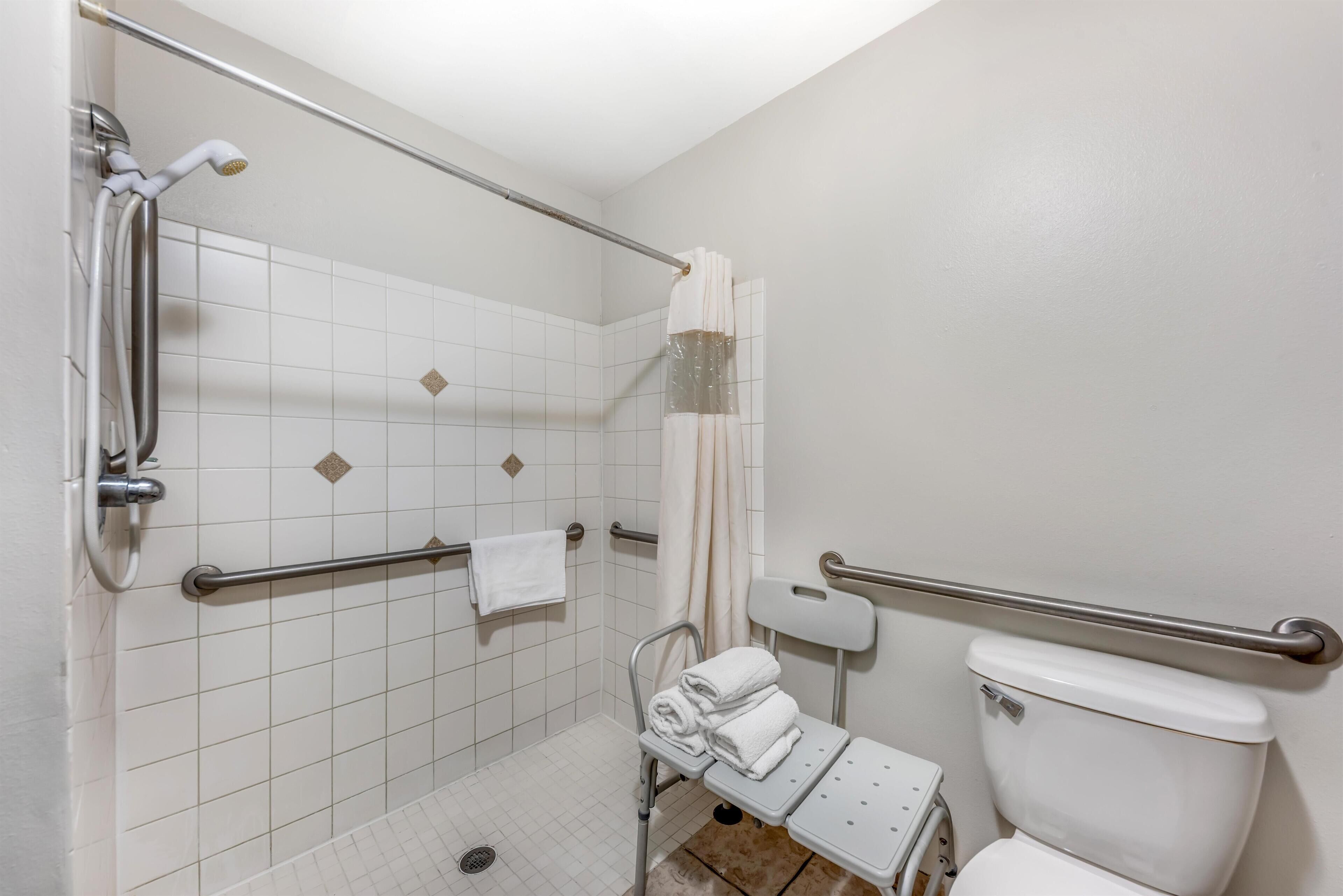 A bathroom with white tiled walls, a white toilet, a shower with a grab bar, and a wheelchair-accessible bench.