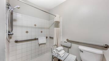 A bathroom with white tiled walls, a white toilet, a shower with a grab bar, and a wheelchair-accessible bench.