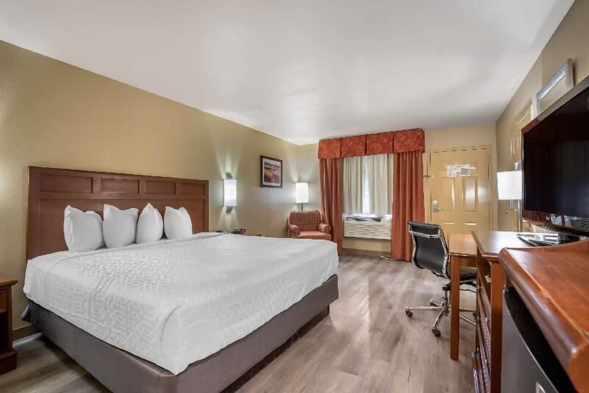 A hotel room with a large bed, a desk, a chair, a television, and a window with curtains.