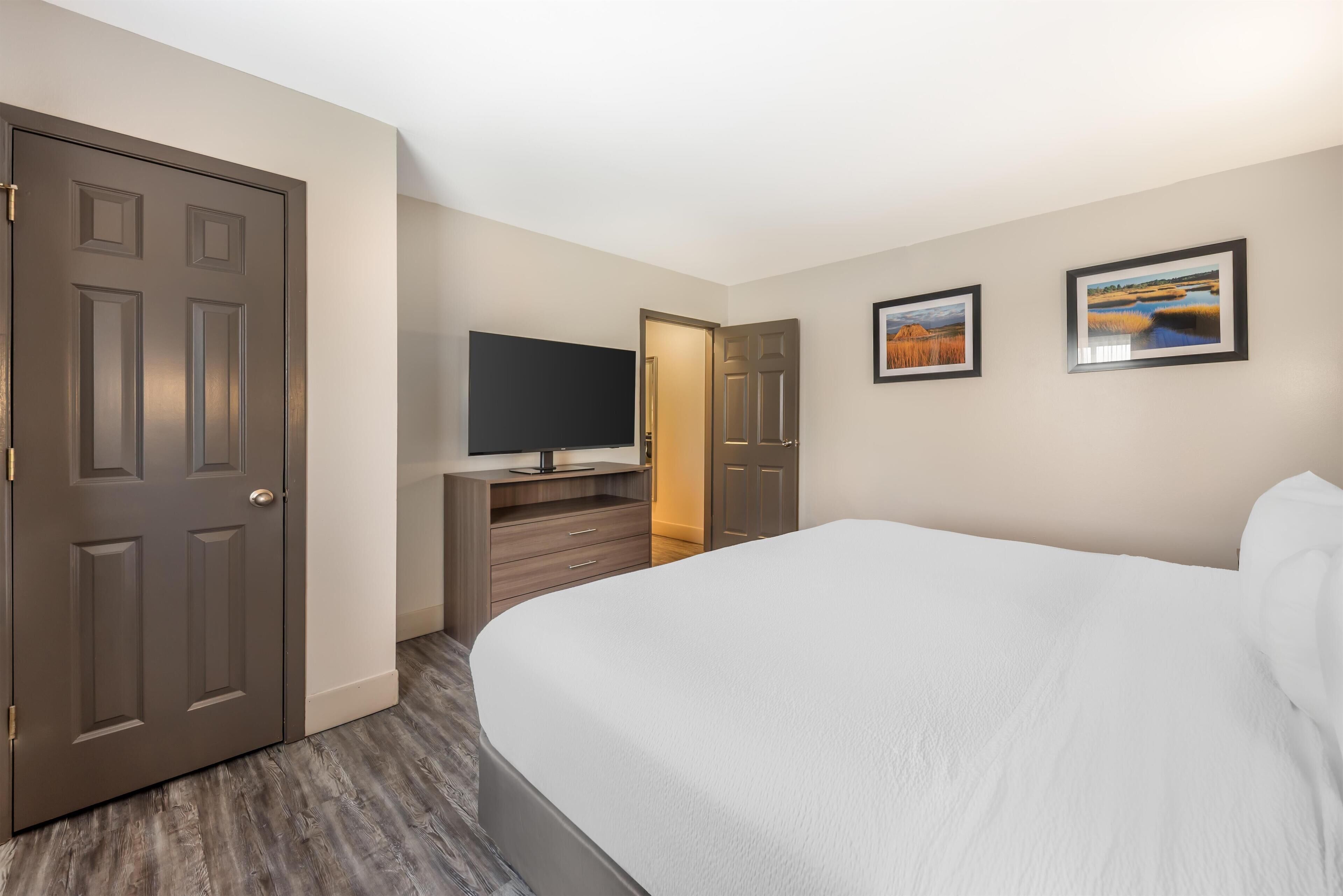 A hotel room with a large bed, a television on a wooden cabinet, and two framed pictures on the wall.