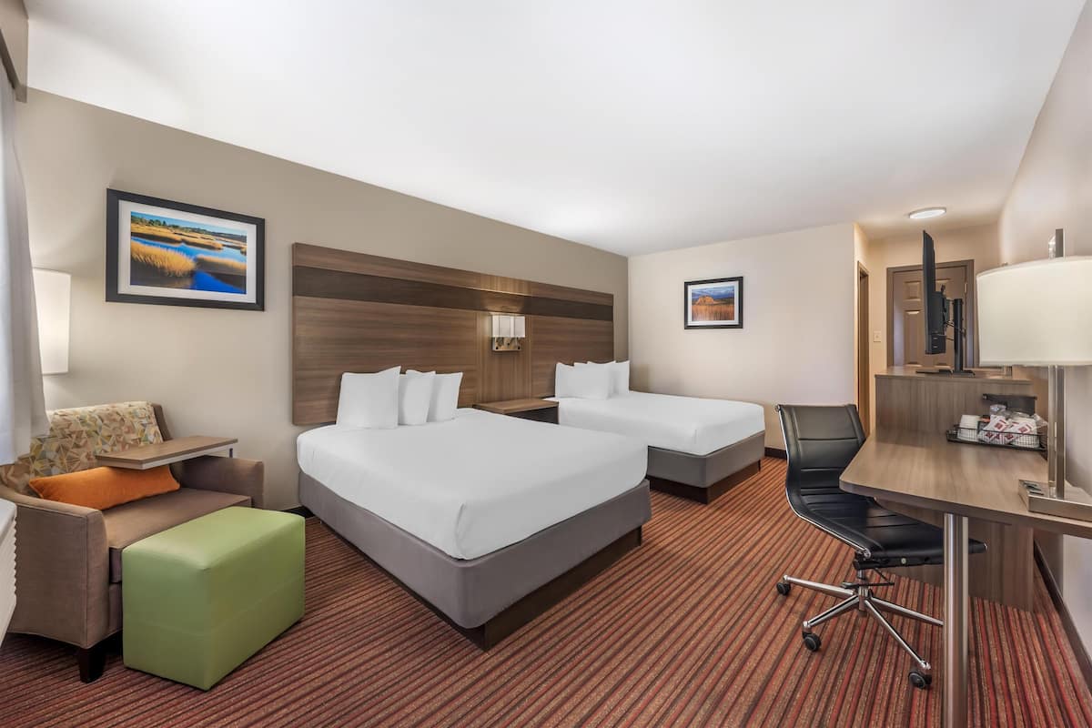 A hotel room with two beds, a desk, a chair, a sofa, and a small table.