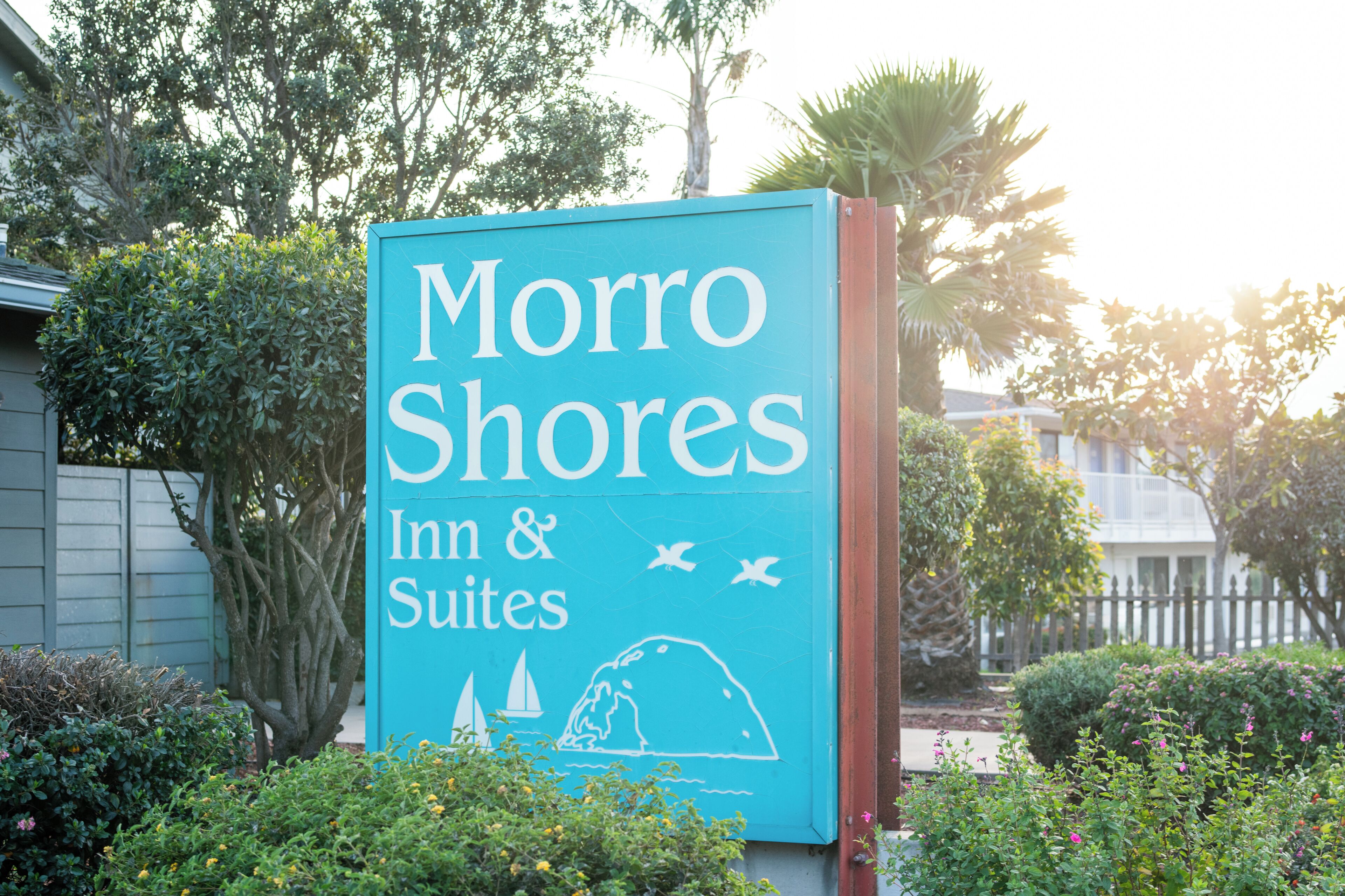 Señal para Morro Shores Inn & Suites con temática náutica, rodeada de vegetación.