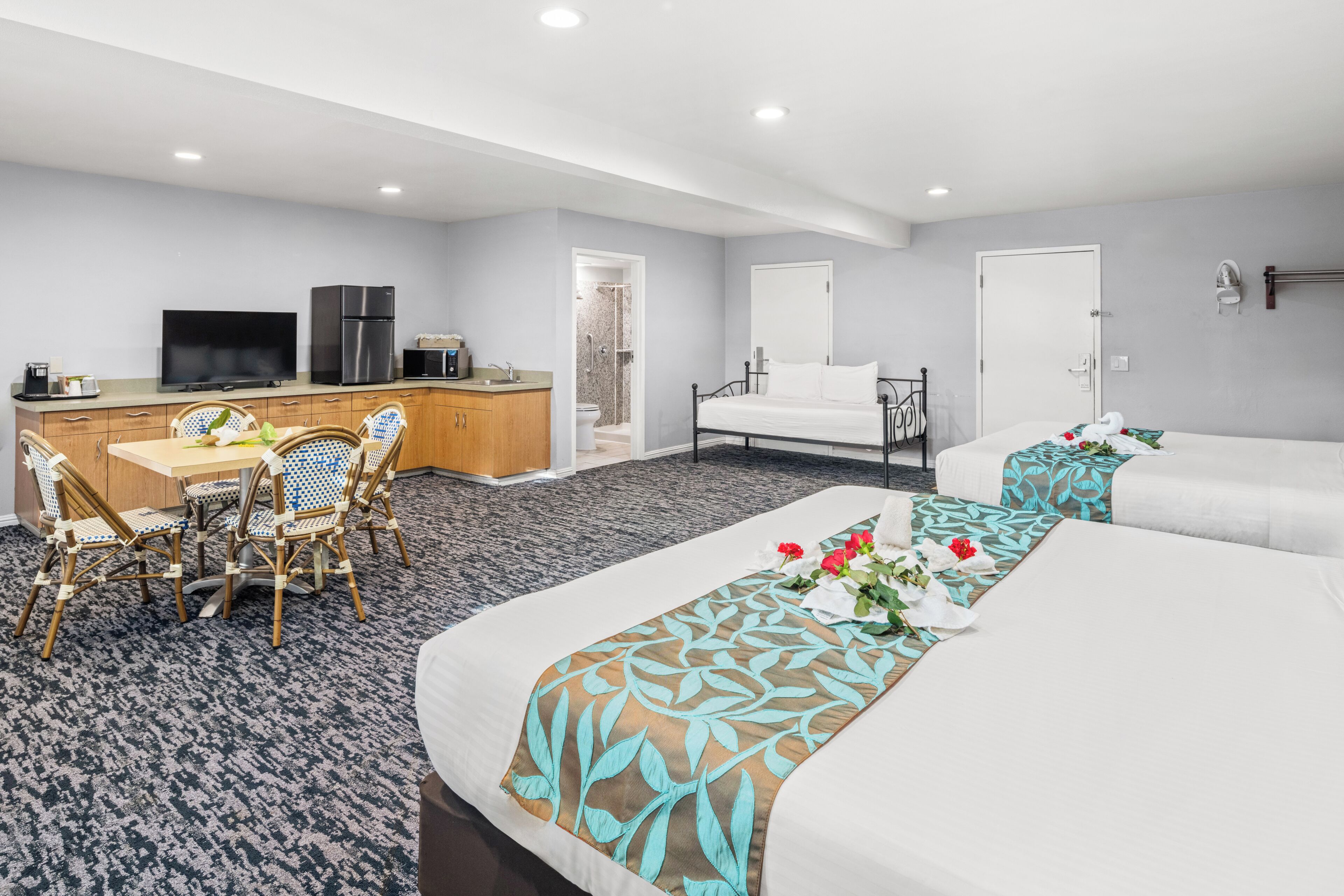 Quarto de hotel com cama, escrivaninha com televisão, cozinha compacta e banheiro.
