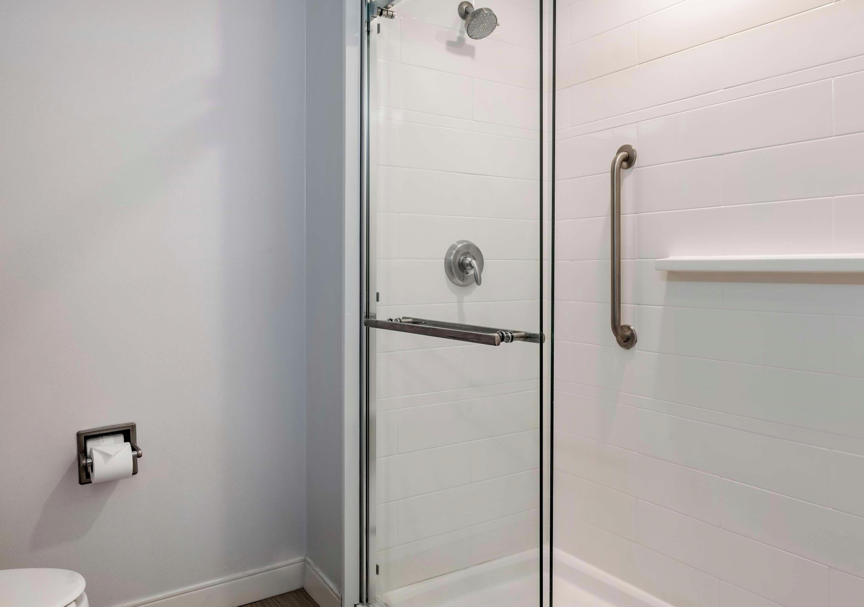 A modern bathroom with a glass shower enclosure, a toilet, and a hand dryer.