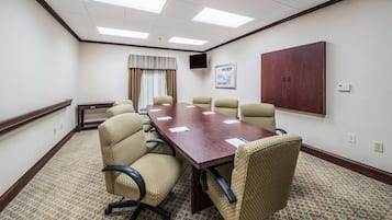Un salón de conferencias con una larga mesa, seis sillas, un televisor y un cuadro en la pared.