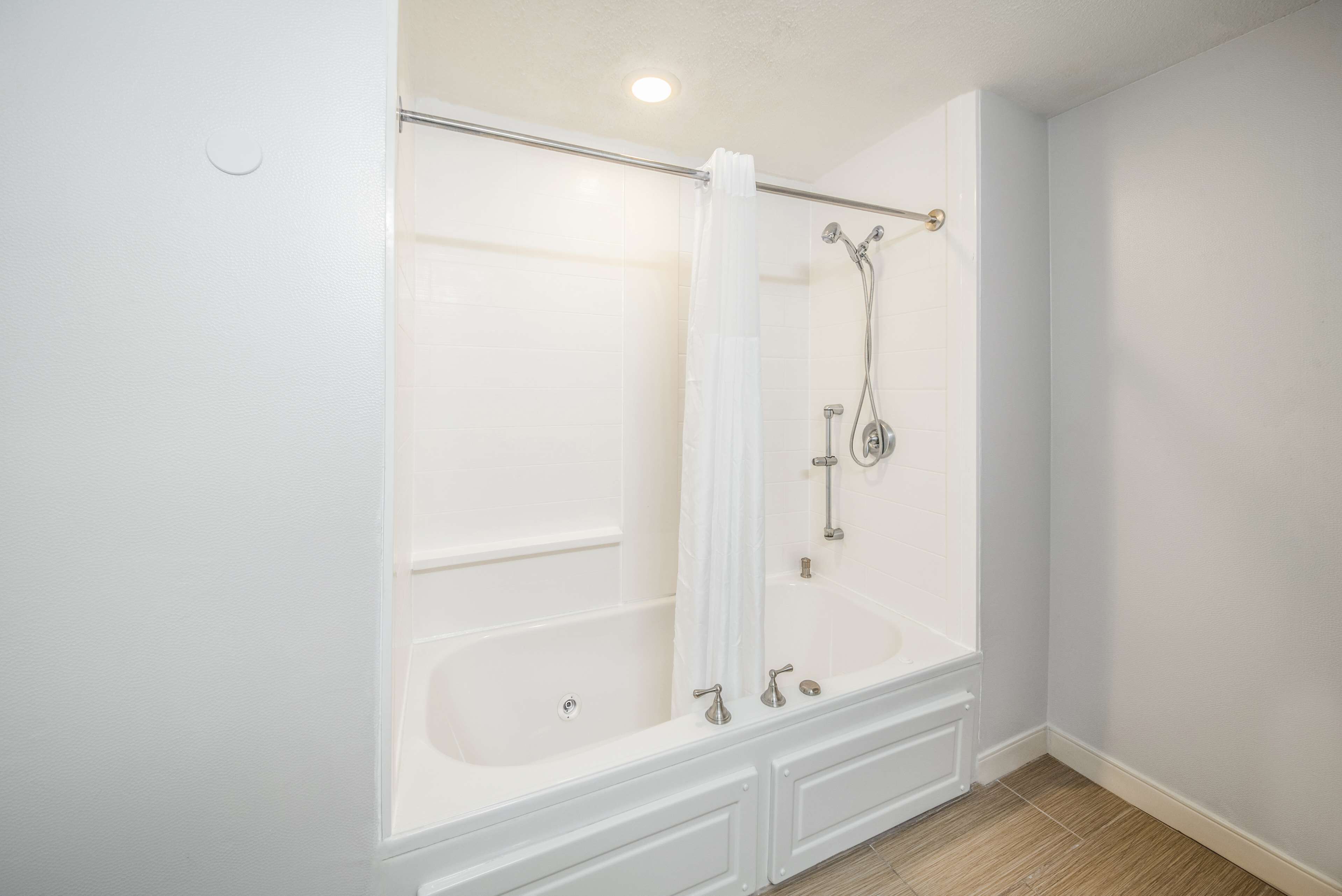 A bathroom with a bathtub, shower, and a white curtain.
