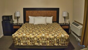 A hotel room with a large bed, two bedside tables, a lamp on each table, a microwave, and an air conditioning unit.