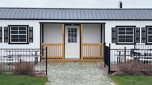 A building with a white exterior, black shutters, and a wooden front door. There is a paved entrance with a small step leading up to the door.