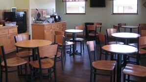 A dining area with multiple tables and chairs, a kitchen area with appliances, and windows with curtains.