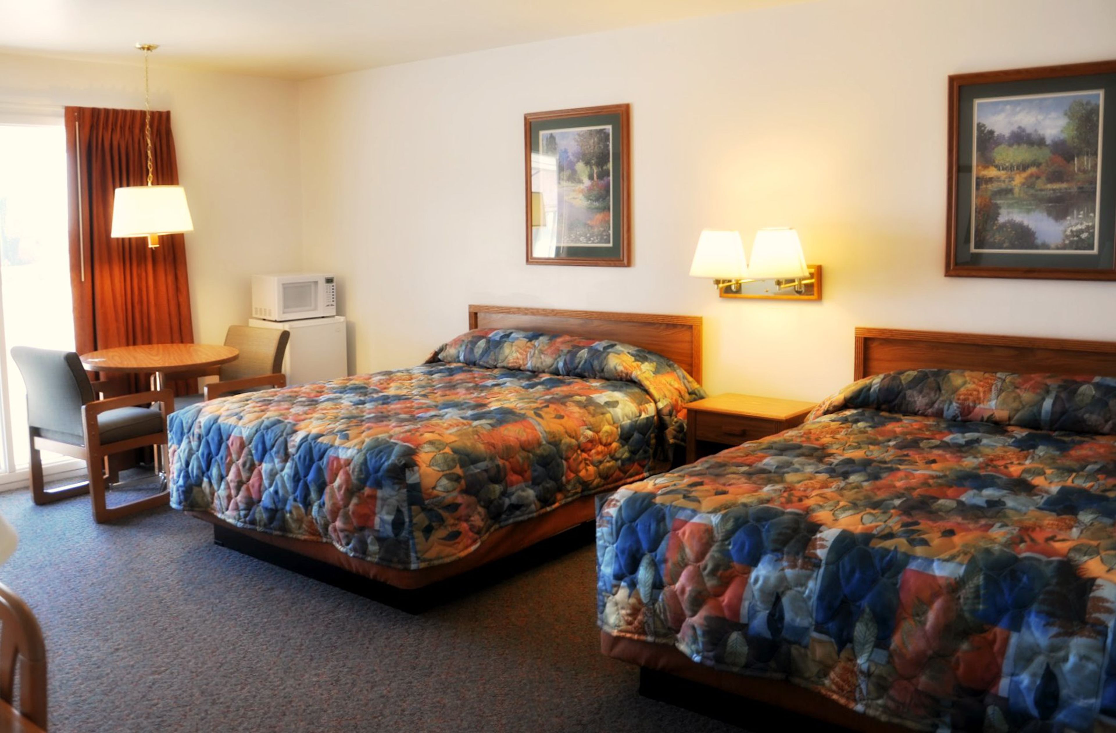 A hotel room with two beds, a desk, a chair, and a television.
