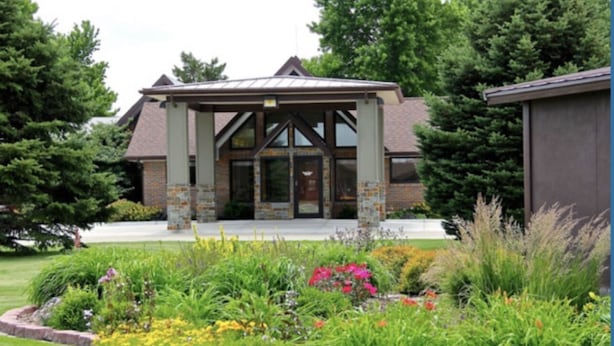 A building with a stone facade, a covered entrance, and a garden with various plants and flowers.