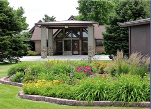 A building with a stone facade, a covered entrance, and a garden with various plants and flowers. - Trade Winds Motel (Valentine)