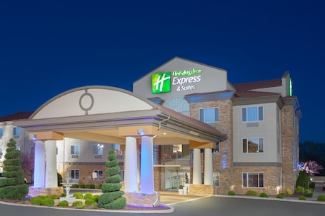 A Holiday Inn Express & Suites building with a covered entrance, multiple floors, and a well-lit facade.