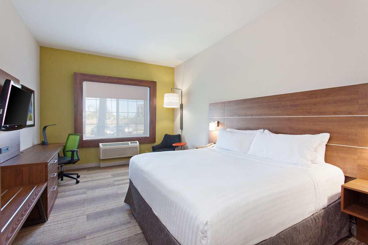 A hotel room with a large bed, a desk with a computer, a chair, a window, and a lamp.