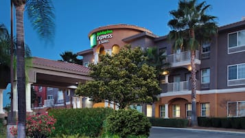 Een Holiday Inn Express & Suites hotel met een gebogen gevel, palmbomen en een rode brandgang-rand.