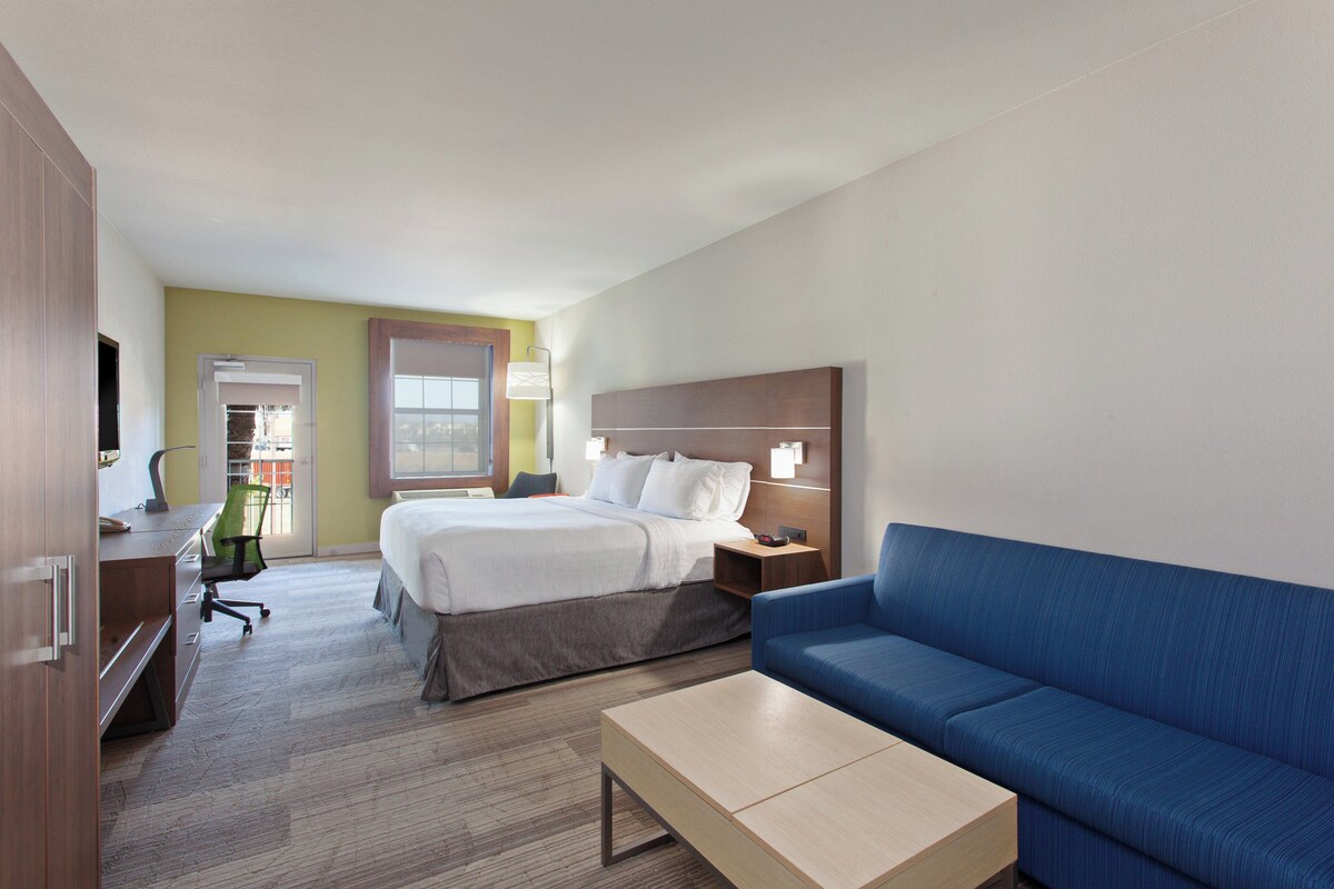 A hotel room with a bed, a blue sofa, a wooden desk, and a lamp.