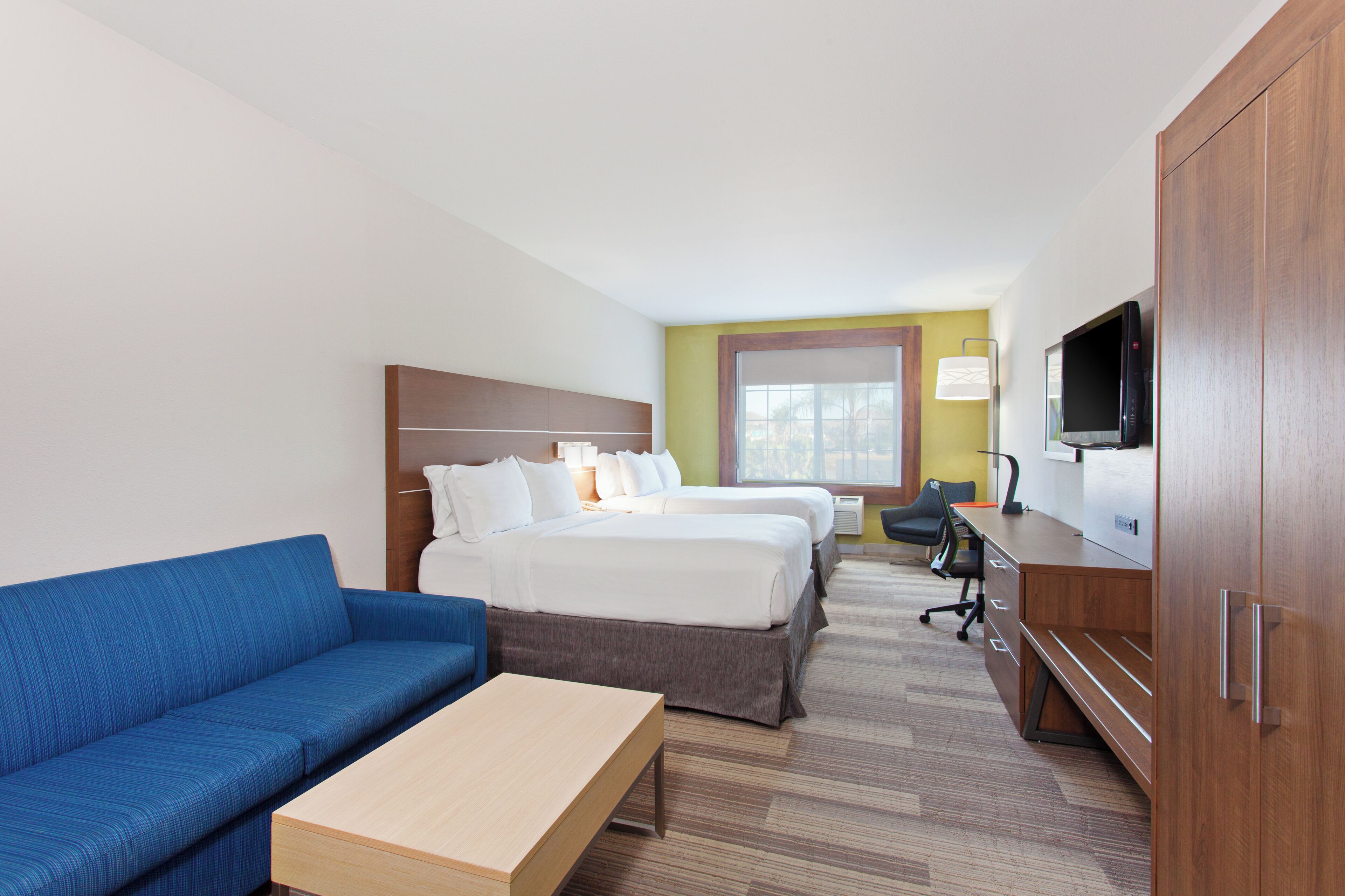 A hotel room with a bed, a blue sofa, a wooden desk, a television, and a window.