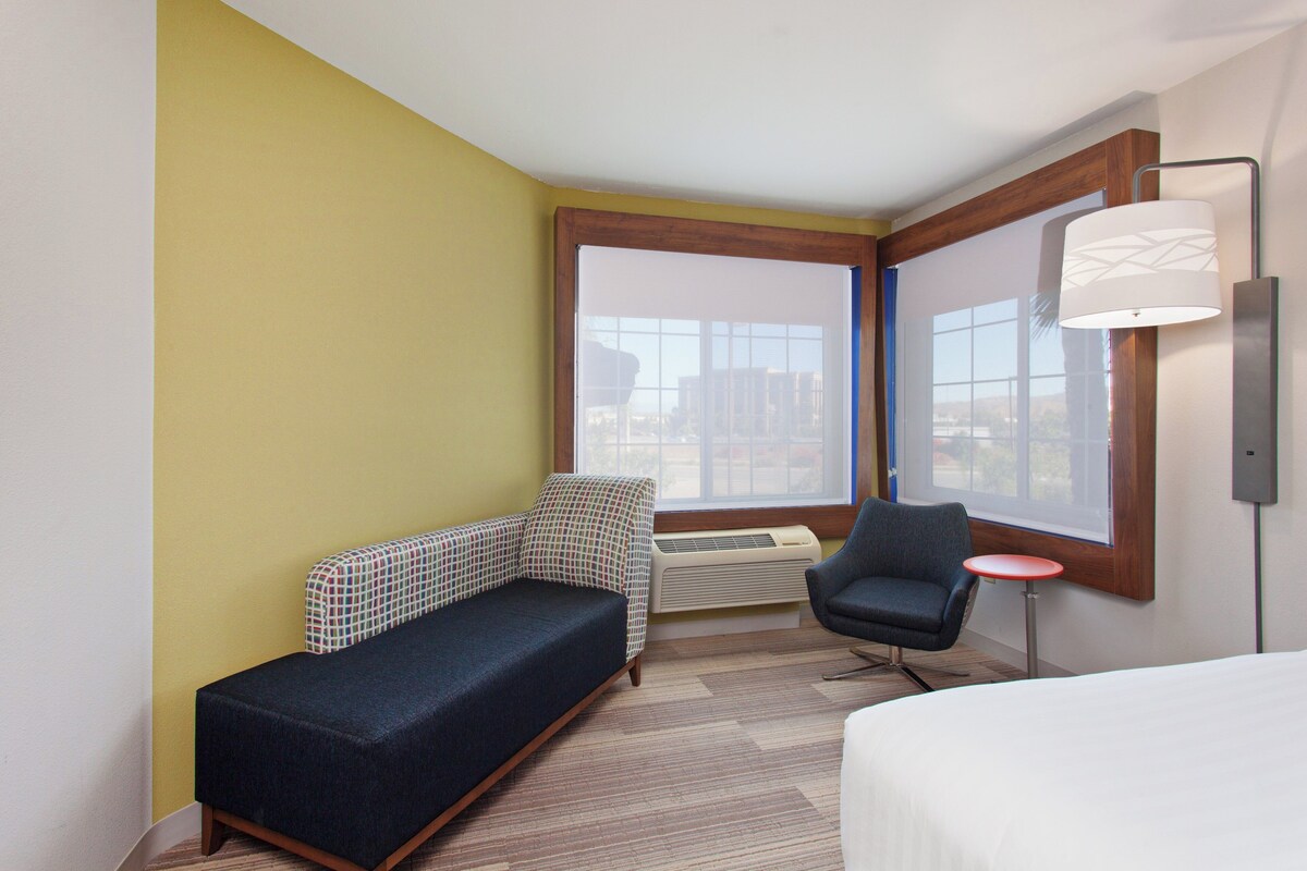 A hotel room with a sofa, a chair, a bed, a window, and a lamp.