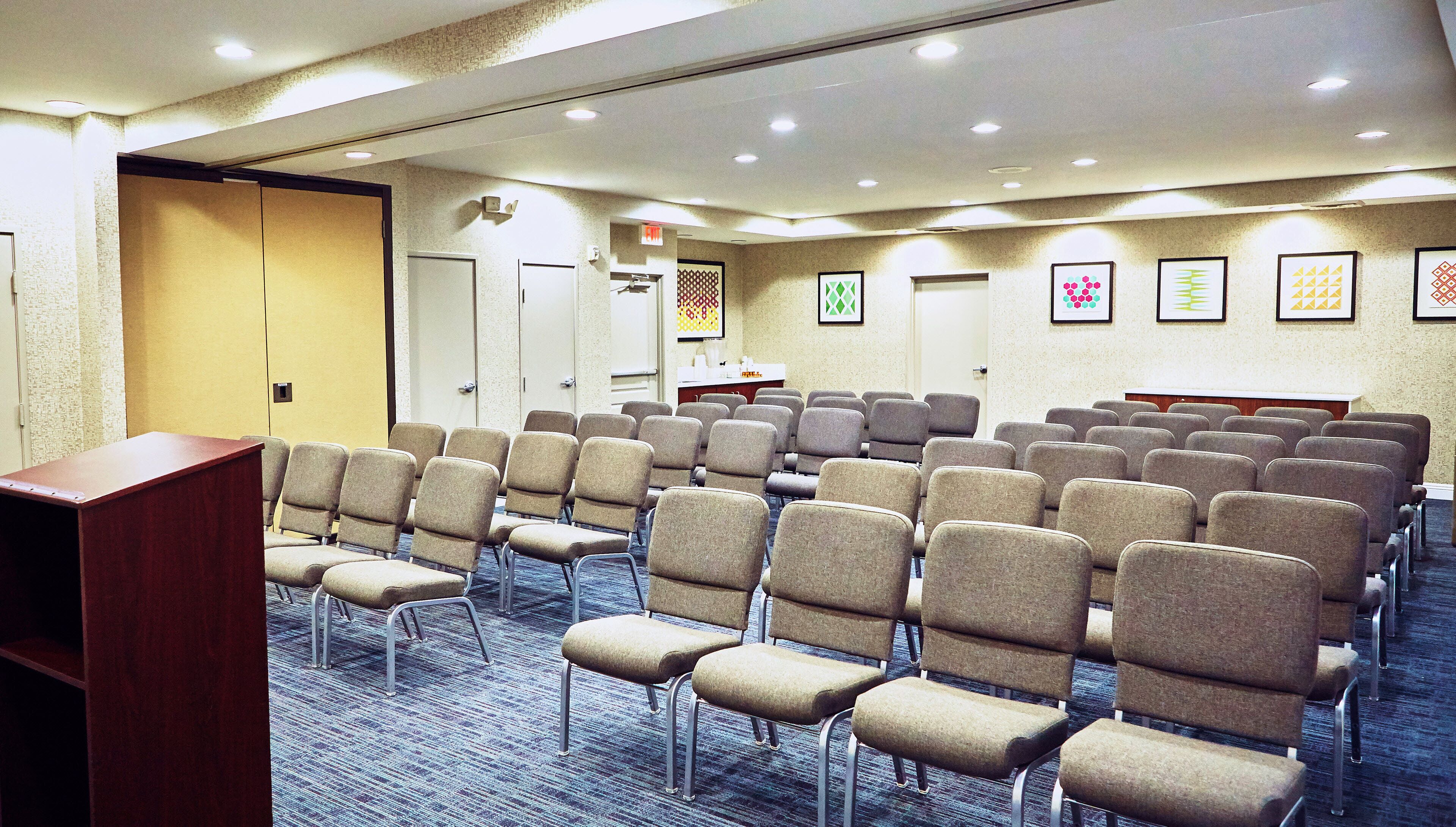 A conference room with rows of chairs, a podium, and a carpeted floor.