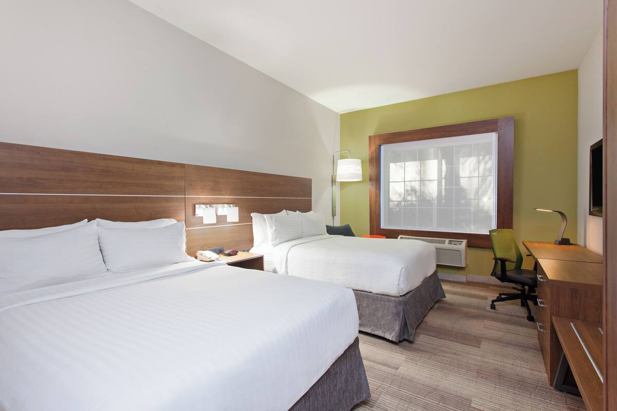 A hotel room with two beds, a desk, a chair, and a window with blinds.