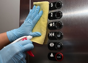 A person cleaning an elevator control panel with a cloth and spray bottle.