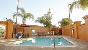 A swimming pool with a sunshade, lounge chairs, and a tiled deck. - Holiday Inn Express & Suites Corona by IHG (Corona)