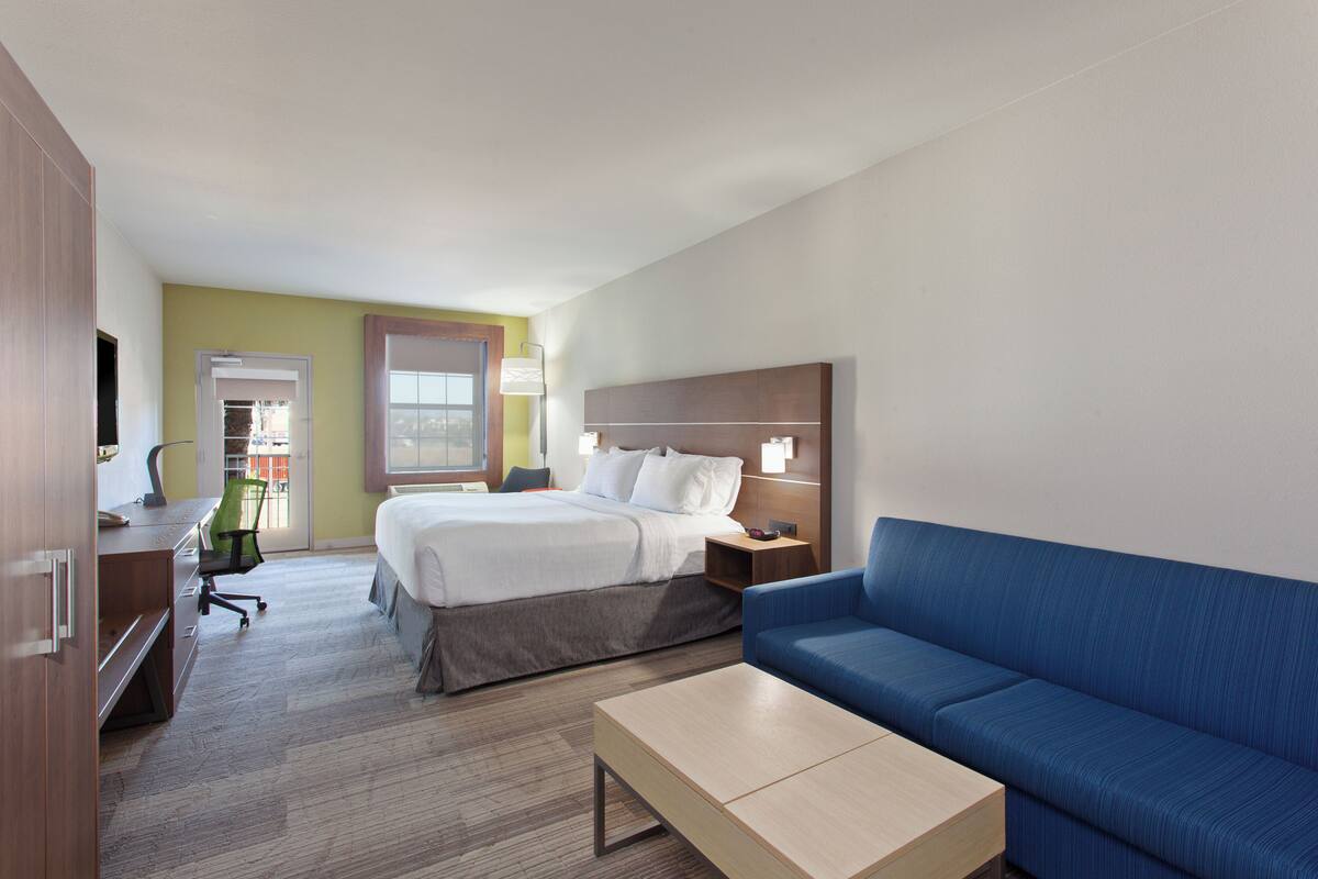 A hotel room with a bed, a blue sofa, a desk with a chair, a lamp, and a television.