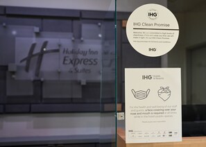 A glass partition with a Holiday Inn Express sign and two IHG Clean Promise posters. - Holiday Inn Express & Suites Corona by IHG (Corona)