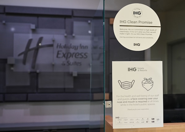 A glass partition with a Holiday Inn Express sign and two IHG Clean Promise posters.