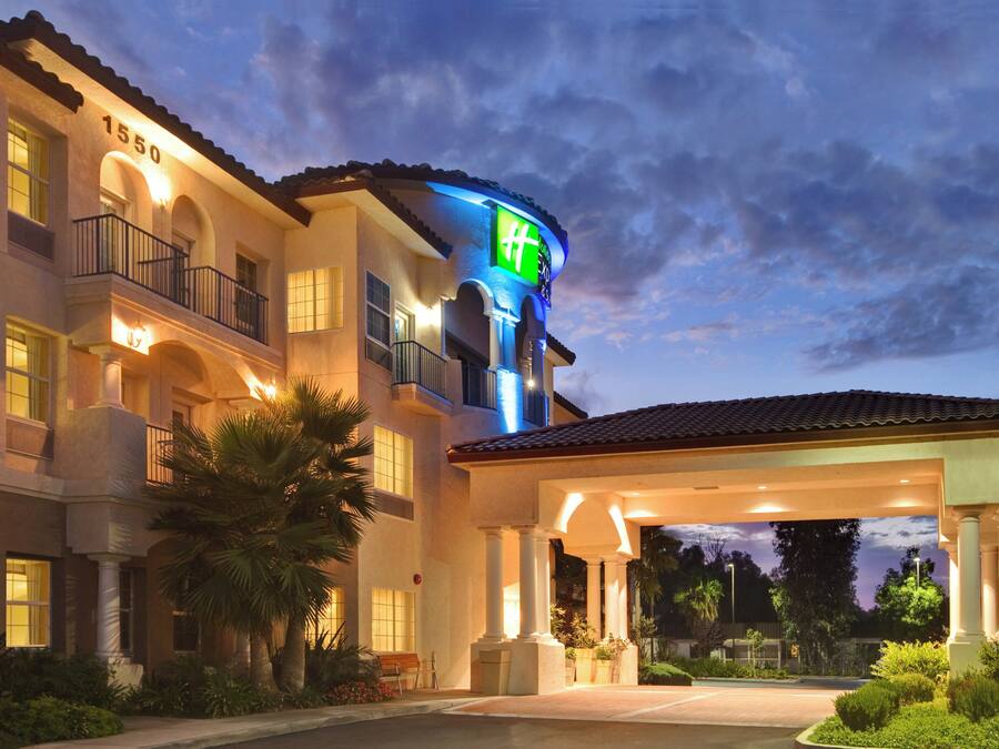 A hotel with a well-lit entrance, multiple balconies, and a covered parking area.